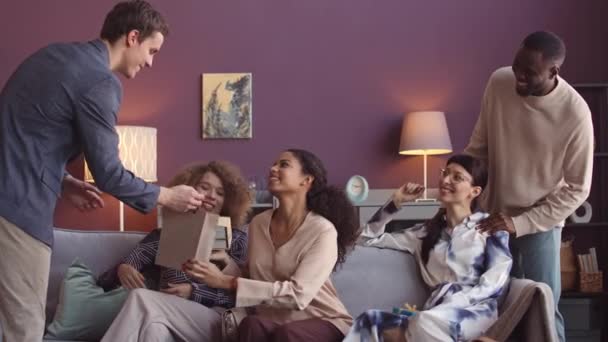 在现代化的公寓里举行舒适的家庭聚会 坐在客厅的沙发上聊天和交换礼物 一群年轻的多民族朋友快乐地聚在一起 — 图库视频影像