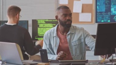 Genç Afrikalı Amerikalı bir adam bilgisayar monitörüne etiket yapıştırırken aynı zamanda meslektaşı bilişim ofisinde yeni bir yazılım programı üzerinde çalışıyor.