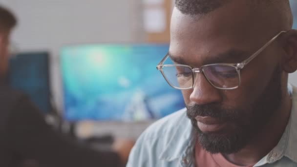 コンピュータゲームを開発しながらキーボードに入力する眼鏡のアフリカ系アメリカ人男性 同僚とオフィスで働く — ストック動画