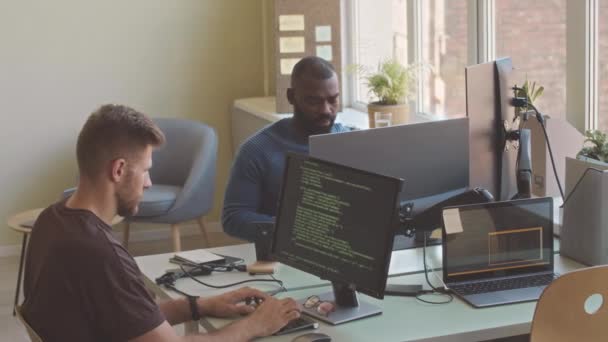 現代オフィスの仕事の間にデスクトップのコンピュータでプログラミングする2人の多民族ソフトウェアエンジニア — ストック動画