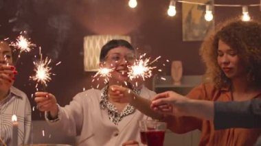 Bir grup mutlu arkadaş, Noel yemeği sırasında sıcak bir evde havai fişek yakıyor.