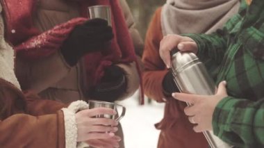Kışın dışarıda sıcak vakit geçirmek için termostan sıcak çay içen bir grup çok ırklı arkadaş.