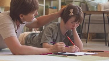 Down sendromlu mutlu bir kız ve şefkatli annesi evde birlikte çizim yapıyor.