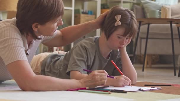 Счастливая Девушка Синдромом Дауна Заботливая Мать Лежащая Дома Ковре Рисуют — стоковое видео