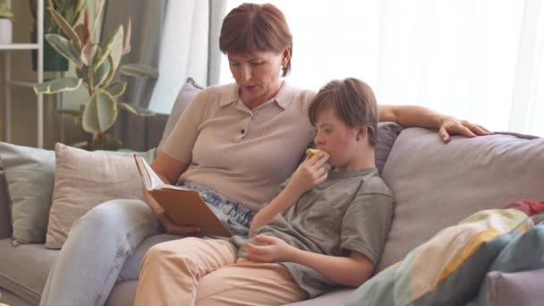 妈妈坐在舒适的客厅里的沙发上 为女儿读那本关于唐氏综合症的书 — 图库视频影像