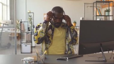 Genç Afrikalı Amerikalı çağrı merkezi çalışanının portresi. Kulaklık takıyor. Ofis masasında oturuyor ve kameraya bakıyor.