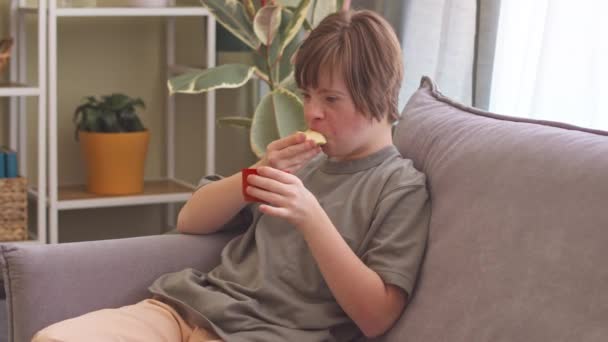 Caucásico Chica Con Síndrome Comer Manzana Sofá Mientras Que Pasar — Vídeo de stock