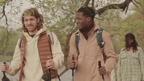 ウォーキングポールとガールフレンドの2人の多様な若い男性の会社 ノルディックは春に公園を歩き 会話をする — ストック動画