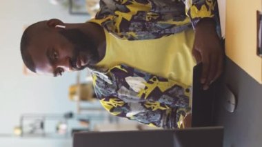 Ofisteki masaüstü bilgisayarında ekiple çevrimiçi video görüşmesi yaparken Afrikalı Amerikalı erkek pazarlama departmanı çalışanının dijital tablet kullanırken dikey görüntüsü