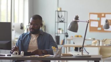 Afrika kökenli Amerikalı iş adamının masaüstü bilgisayarının başında otururken kablosuz kulaklıkla proje detaylarını tartışırken PAN görüntüsü