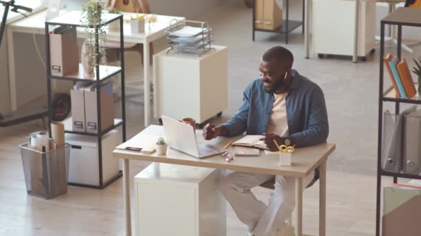 年轻的黑人和他的同事一起坐在现代办公室的白桌前 坐在笔记本电脑上 — 图库视频影像