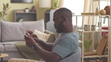 Evde dijital tablet kullanırken kameraya gülümseyen gözlüklü Afrikalı Amerikalı bir adamın portresi.