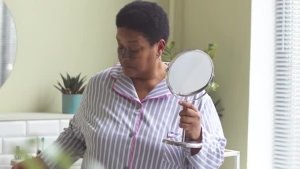 Mujer Afroamericana Mediana Edad Pijama Mirando Espejo Mientras Aplica Máscara — Vídeo de stock