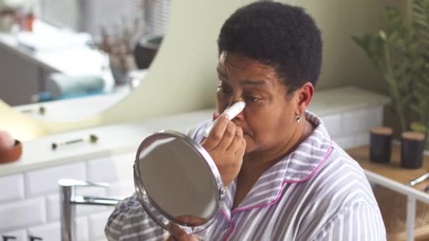 在浴室做日常皮肤护理时 成熟的非洲裔美国妇女在眼皮底下涂防肿凝胶 — 图库视频影像