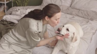 Güzel, beyaz kadın, hafta sonu yatağında köpeğiyle oynayan ipek pijamalı.