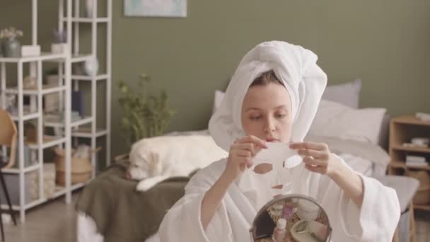 코카서스 여성은 아름다움 루틴을하고 침실에서 마스크를 적용합니다 배경에서 침대에 라브라도 — 비디오