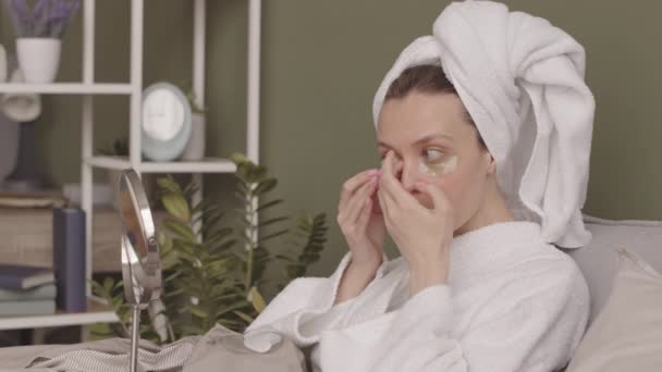 Ung Vit Kvinna Handduk Huvudet Applicera Ögonlappar När Sitter Sängen — Stockvideo