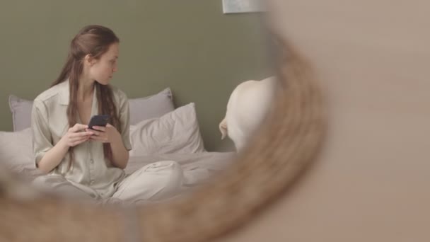 Дівчина Затишній Піжамі Смс Смартфон Відпочиваючи Ліжку Своєю Собакою Лінивий — стокове відео