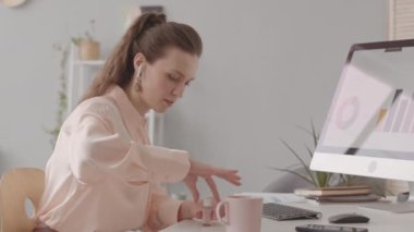 Masa başındaki bilgisayarla tırnaklarını boyayan beyaz bir kadın.