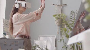 VR kulaklık takan genç bir kadın işyerinde sanal gerçekliği yaşarken elleriyle hareket ediyor.