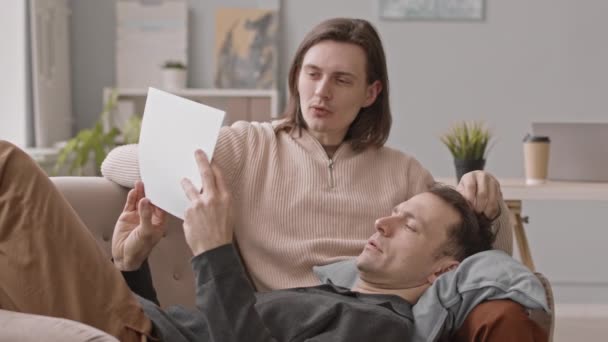 手里拿着商业文件的男人慢吞吞地躺在男朋友身边讨论着工作 — 图库视频影像