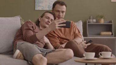 Romantik eşcinsel çift oturma odasında dinleniyor. Akıllı telefondan video izliyorlar.