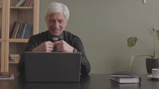成年灰发牧师 身穿黑色衬衫 手持念珠 通过笔记本电脑上的视频通话 与教区居民交谈 — 图库视频影像