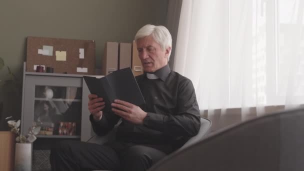 Старший Священник Черной Рубашке Белом Воротничке Читает Библию Вслух Дома — стоковое видео
