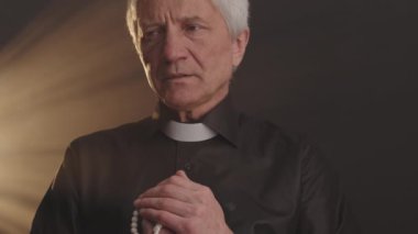 Kilisede dua ederken elinde tespih taşıyan, siyah gömlekli, beyaz yakalı, gri saçlı papaz.