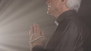 Dua eden elleriyle Tanrı 'yla konuşan, karanlık kilisedeki parlak ışığa bakan kıdemli rahibin yavaşlığı.
