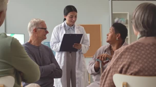 在疗养院与多族裔老年人交谈的带剪贴板年轻女护士 — 图库视频影像