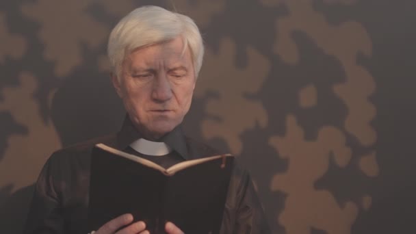 黒いシャツと白い聖職者カラーのシニア牧師のスローモーは 聖書を読んで上を見ながらバラのビーズを保持しています — ストック動画
