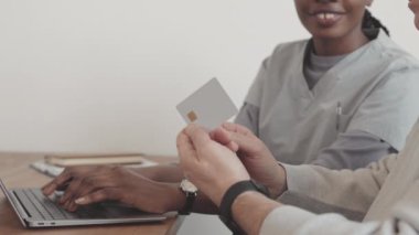 Genç Afrikalı Amerikalı kadın sosyal hizmet görevlisinin yardımıyla internetten alışveriş yapmayı öğrenirken kredi kartını elinde tutan Kafkas ihtiyarının yavaşlığı.