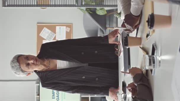 彼女のチームとのブリーフィングミーティングをしながら オフィスのテーブルの頭に立っている成功した成熟したアジアのビジネスマンの垂直ショット — ストック動画