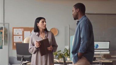 Çağdaş ofiste durmuş sohbet eden genç meslektaşlar.