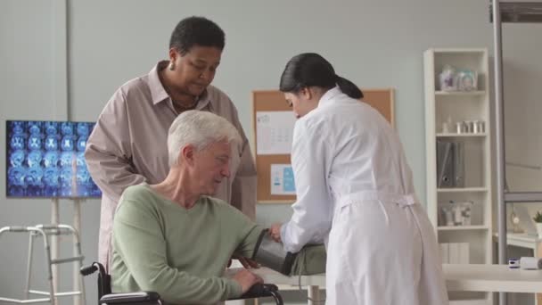 診療所の診察予約中に高齢者の血圧を測定する女性看護師 — ストック動画