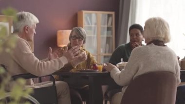 Yaşlılardan oluşan etnik çeşitlilikte bir grup huzurevindeki yemek masasında sohbet ediyorlar.