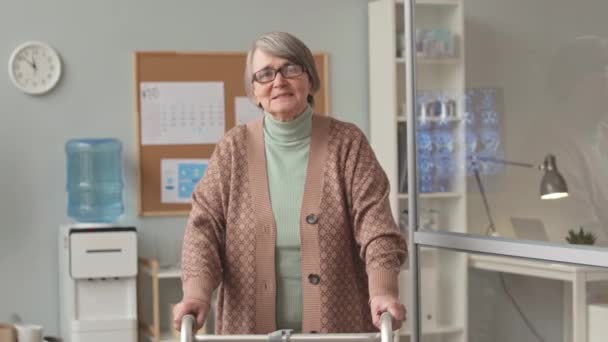 站在医生办公室前 照片中带着微笑的灰白头发 头戴步行机的老年妇女站在镜头前 — 图库视频影像