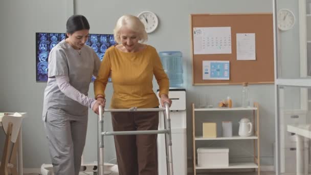 Νεαρή Νοσοκόμα Ποδιά Βοηθά Ηλικιωμένη Γυναίκα Περπατήσει Κατά Μήκος Του — Αρχείο Βίντεο