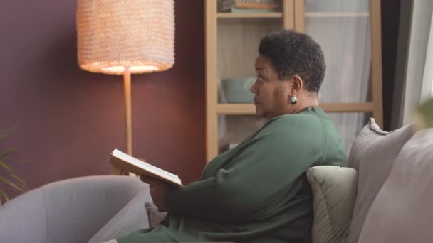 Przyjazna Młoda Pielęgniarka Rozmawia Afroamerykanką Czytającą Książkę Kanapie Domu Opieki — Wideo stockowe