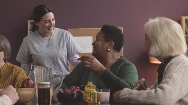 年轻快乐的护士在灌木丛中与不同的老年人聊天 坐在养老院的餐厅里 — 图库视频影像