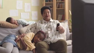 Afro-Amerikalı büyükanne iki torunuyla evde vakit geçirirken TV 'de kanal değiştiriyor.