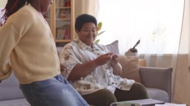 İki tatlı Afrikalı Amerikalı ergen kardeş, oturma odasında kanepede oturan ve örgü ören büyükannelerine küçük paketlerle hediyeler veriyorlar.