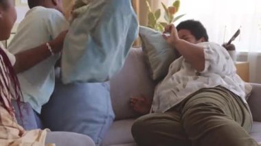 İki oyuncu Afrikalı Amerikalı ergen kardeş ve modern büyükanne yastıkları gündüz vakti oturma odasında kanepede kavga ediyorlar.