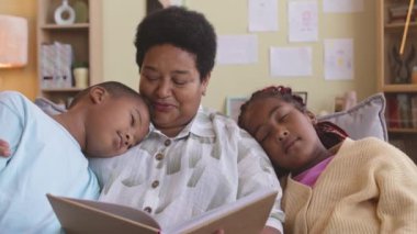 Afrika kökenli Amerikalı büyükanne iki torununa kitap okuyor ve gündüzleri omuzlarında kestiriyor.