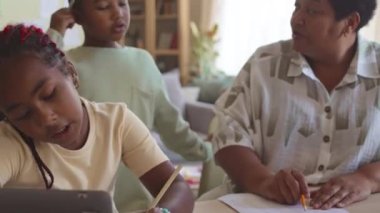 Yetişkin Afro-Amerikalı bir kadın oturma odasında ödev yaparken iki torununa matematik anlatıyor.