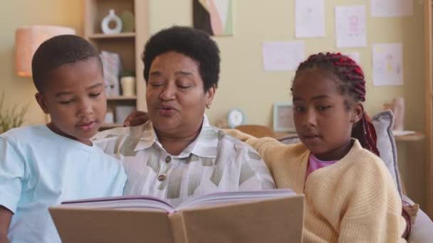Volwassen Zwart Vrouw Voorlezen Boek Naar Haar Tussen Kleinkinderen Zitten — Stockvideo