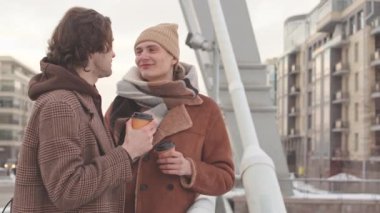 İki beyaz aşık genç adam, kış günü şehirde romantik bir yürüyüş yaparken kahve eşliğinde sohbet ediyorlar.