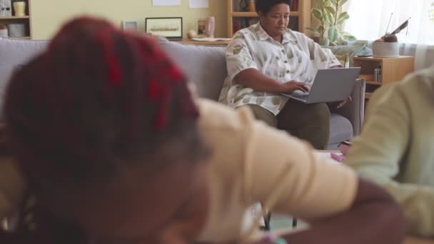 两名非裔美国小学生在家里和祖母一起 用笔记本电脑在沙发上做数学计算 — 图库视频影像