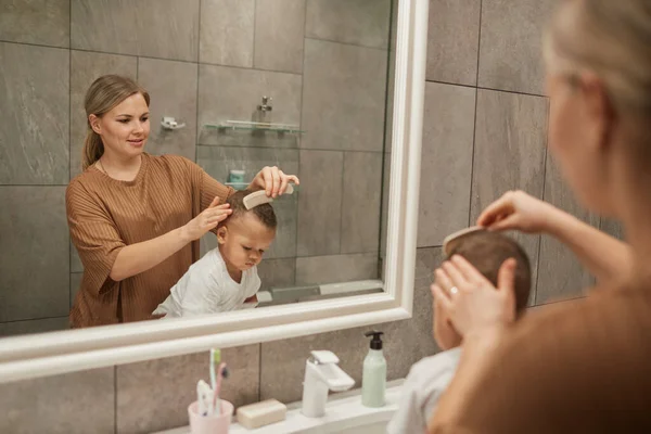 关怀备至的白人母亲在浴室用镜子梳理男婴头发的肖像 复制空间 — 图库照片